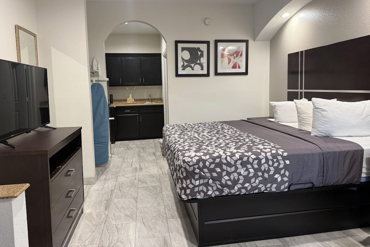A compact hotel room with a bed, a TV, a kitchenette, and a bathroom.