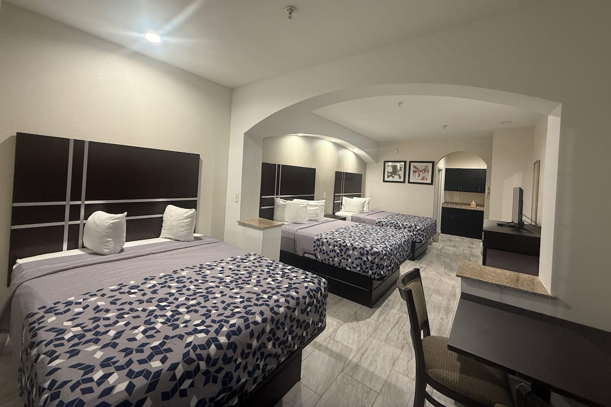 A hotel room with two beds, a desk, and a chair. There is a mirror on the wall and a small table.