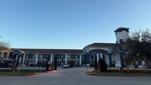 Ein mehrstöckiges Hotel mit Innenhof, einem Glockenturm und einem eingezäunten Parkplatz.