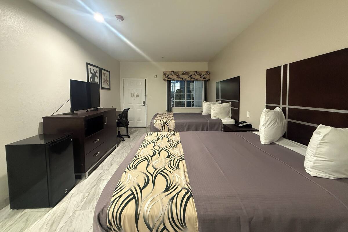 A hotel room with a large bed, a desk with a computer, a television, and a window with a view of buildings.