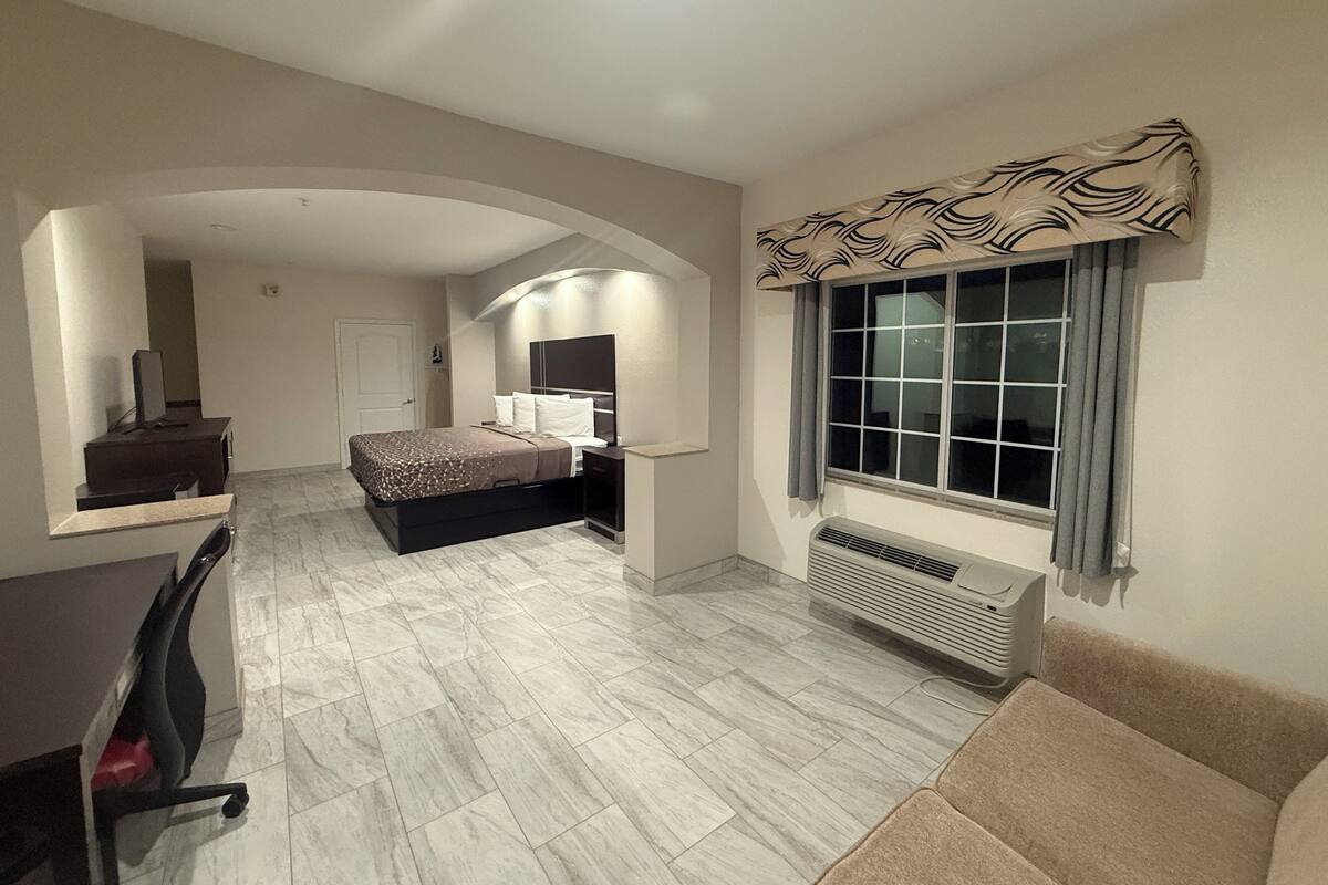 A modern hotel room with a bed, a desk, a chair, a TV, and a window with curtains.