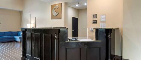 A reception desk with a dark finish, a blue sofa, and a clock on the wall.