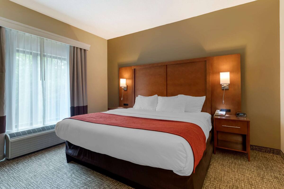 Ein Hotelzimmer mit einem großen Bett, zwei Nachttischlampen, einem Nachttisch und einem mit Vorhängen versehenen Fenster.