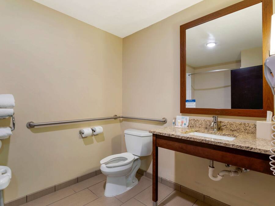A bathroom with a toilet, hand dryer, and handrails.
