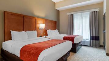 Habitación de hotel con dos camas, cabecero de madera, un ventanal con cortinas y piso alfombrado.