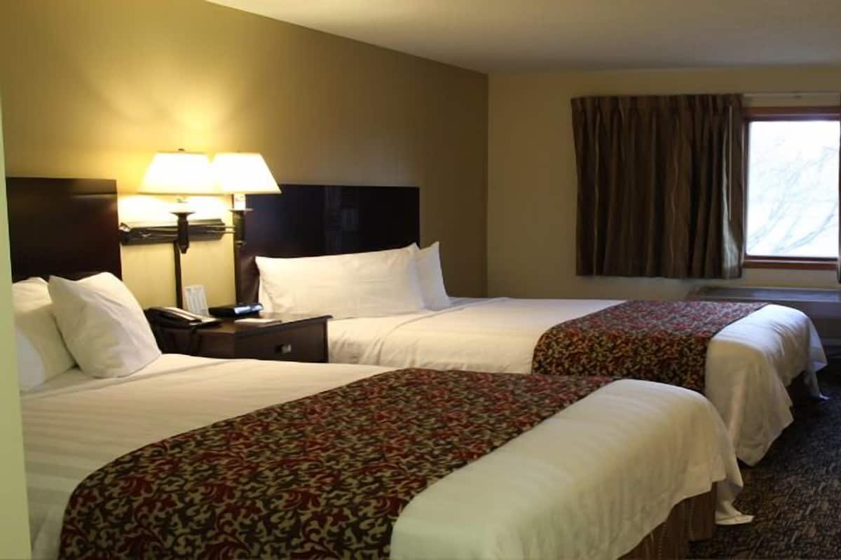 A hotel room with two beds, a desk, a chair, and a window with curtains.