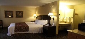 Quarto de hotel com uma cama, duas luminárias de cabeceira, mesa de cabeceira, espelho e pequena escrivaninha com telefone.