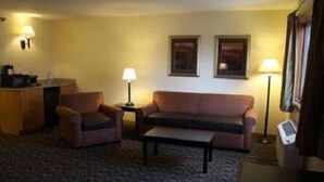 Ein kleiner, gemütlicher Raum mit einer Couch, zwei Sesseln, einem Couchtisch und einem Schreibtisch mit Lampe. An der Wand hängen zwei gerahmte Bilder.