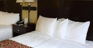 A hotel room with two beds, a nightstand with a lamp, and a dark wooden headboard.