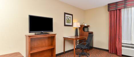 A hotel room with a television, a desk with a chair, a lamp, and a window with curtains.