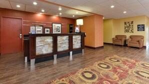 A reception area with a stone counter, framed pictures, a welcome sign, and a carpeted floor. - Hampton Inn Muscatine (Muscatine)