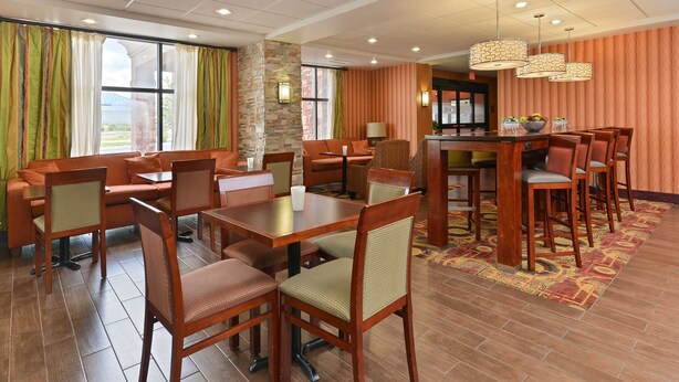 A hotel dining area with wooden furniture, a stone accent wall, and a view of the outdoors. - Hampton Inn Muscatine (Muscatine)