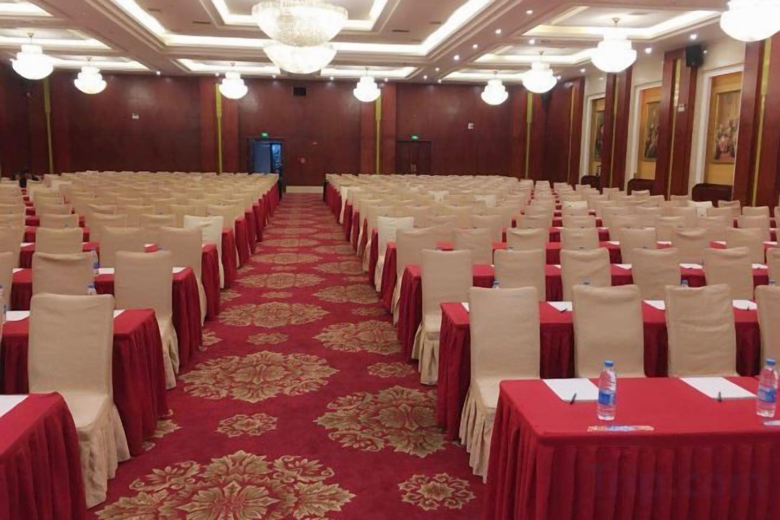 A conference room with rows of tables and chairs, a red carpet, and a chandelier.