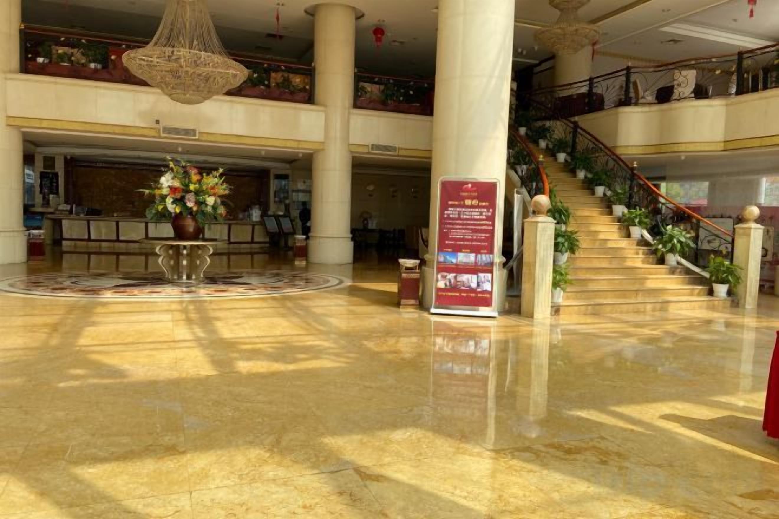 A spacious lobby with a marble floor, a reception desk, a staircase, and a hanging chandelier.