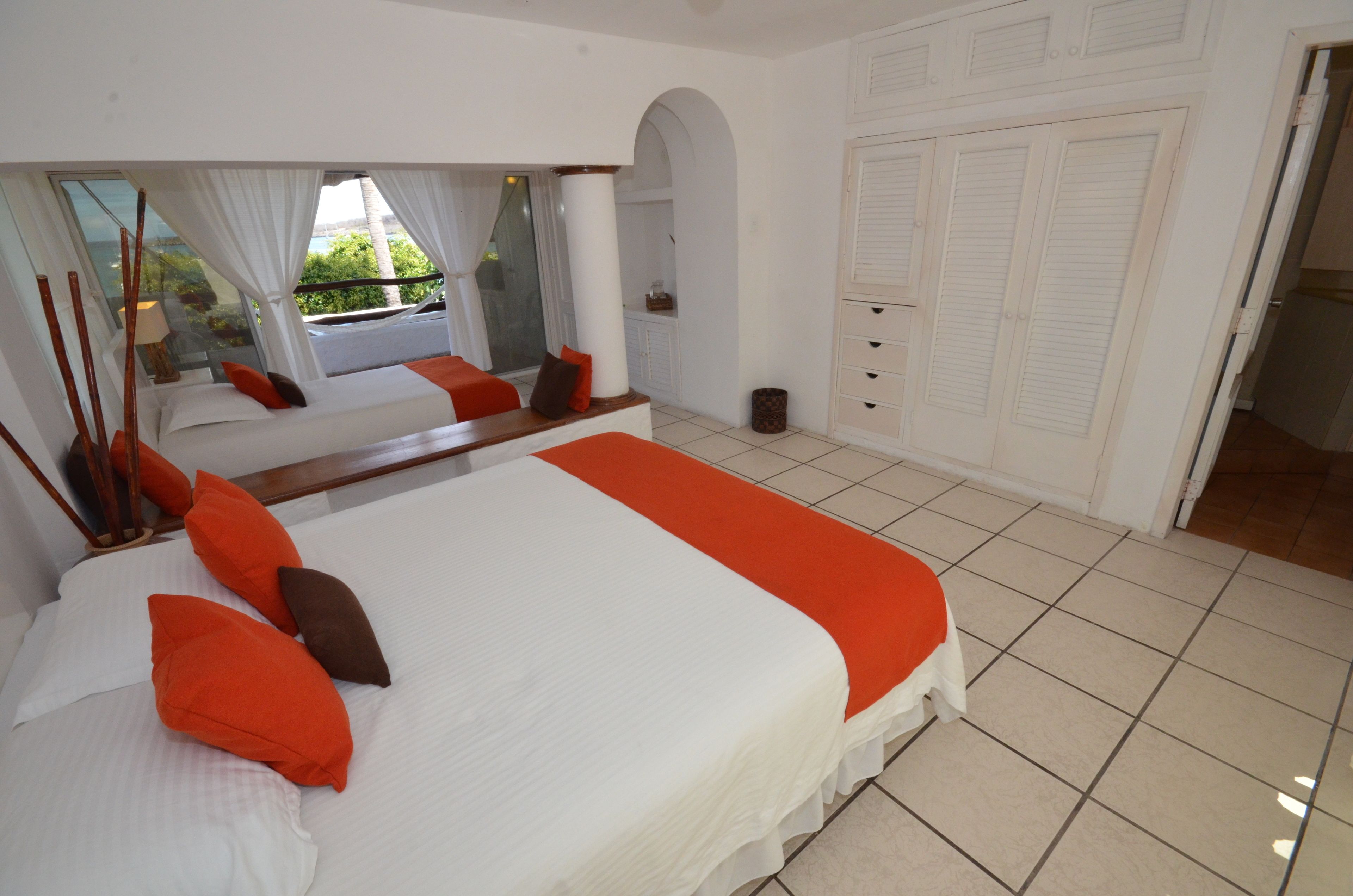 A bedroom with a large bed, a mirror, a window with curtains, and a wardrobe.