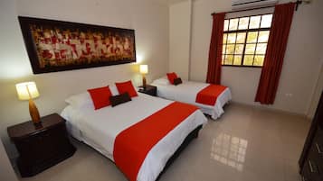 Habitación de hotel con dos camas, una mesita de noche con lámpara, un cuadro grande en la pared y una ventana con cortinas.