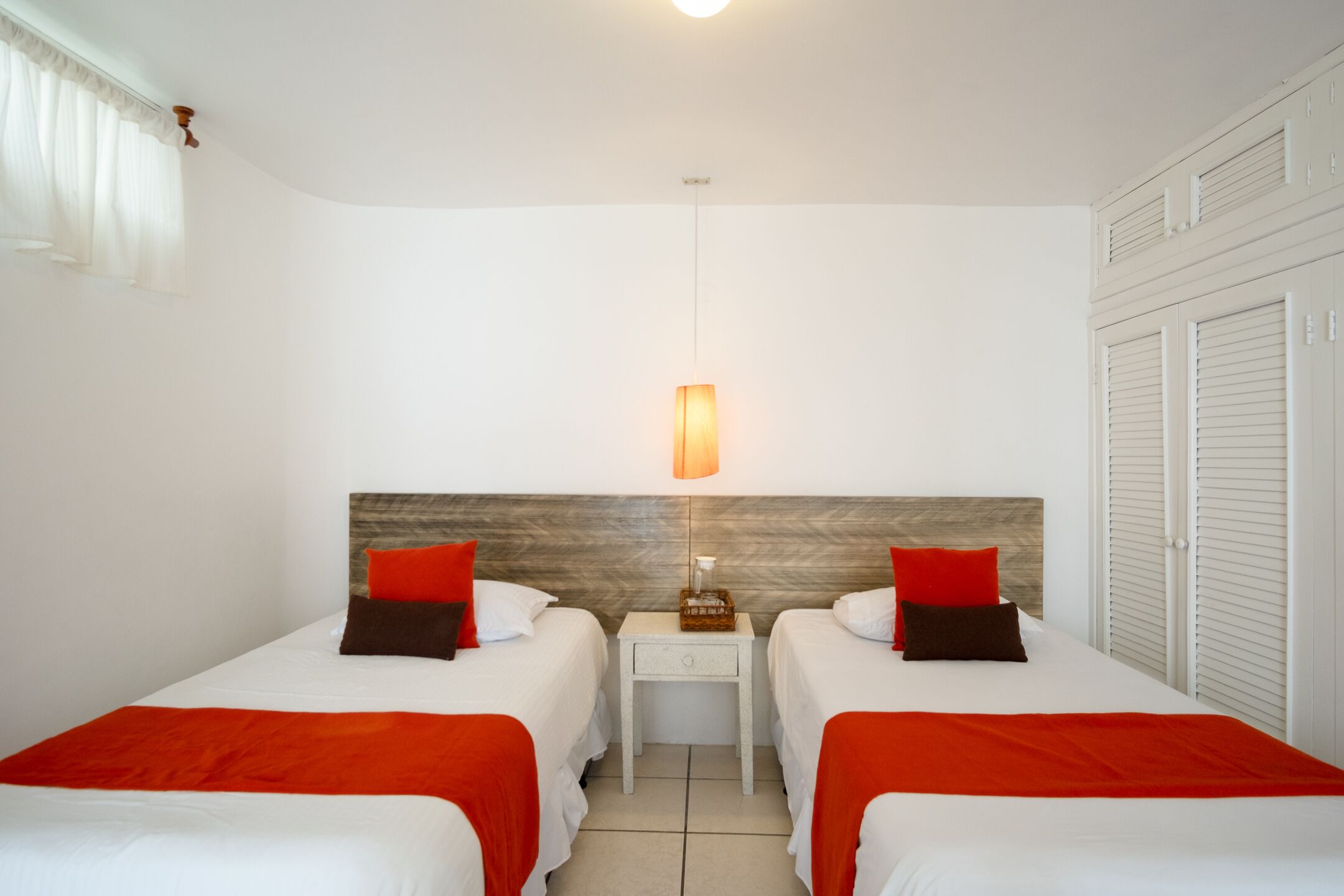 Et hotelværelse med to senge, et natbord, en lampe og et klædeskab.