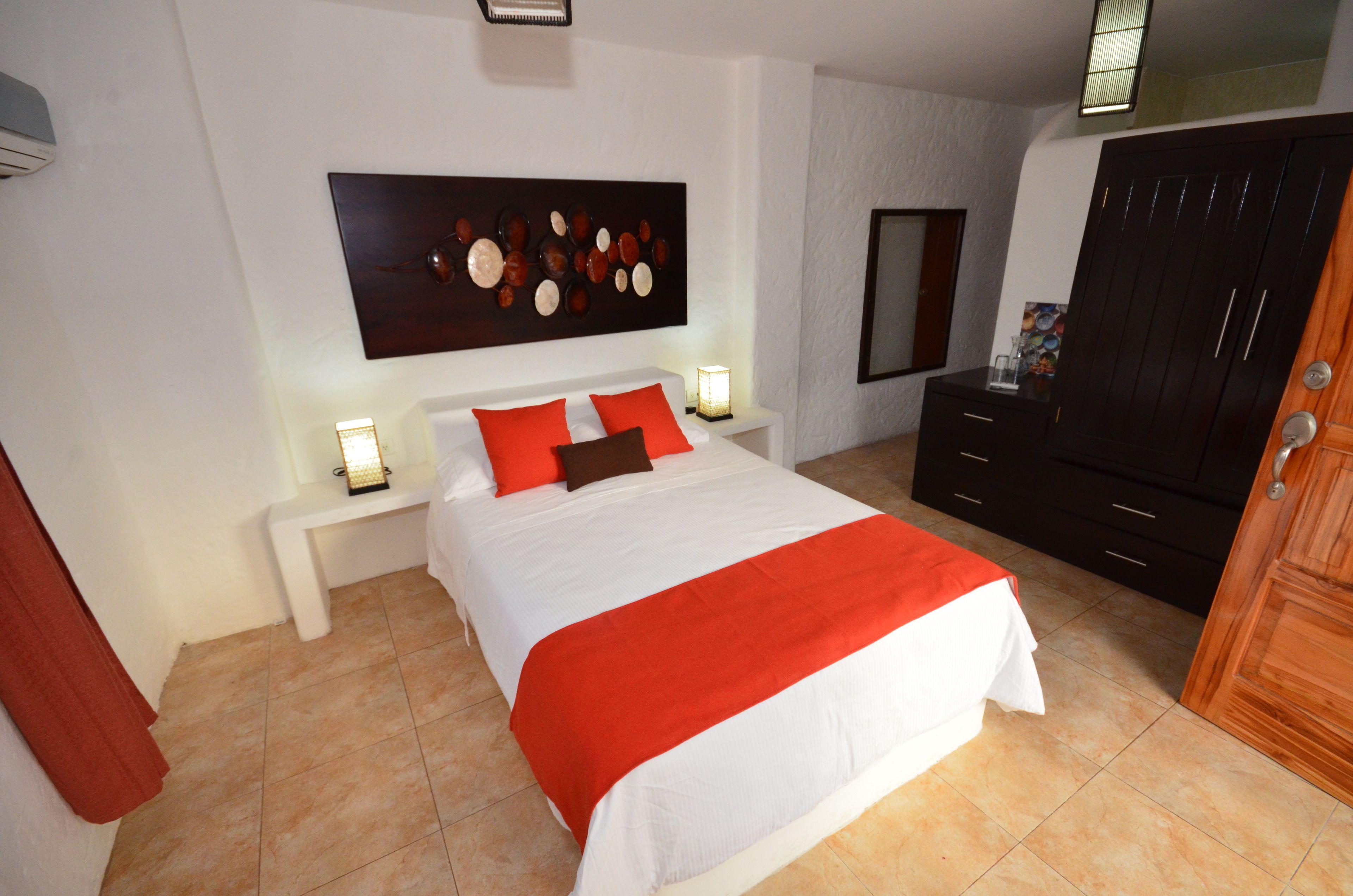 Un dormitorio con una cama grande, una mesita de noche con lámpara, un armario y una obra de arte en la pared.