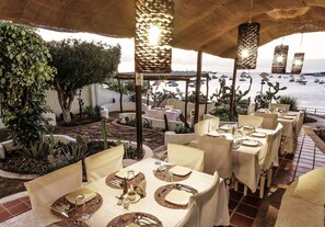 An outdoor dining area with tables set for two, overlooking a body of water with boats.