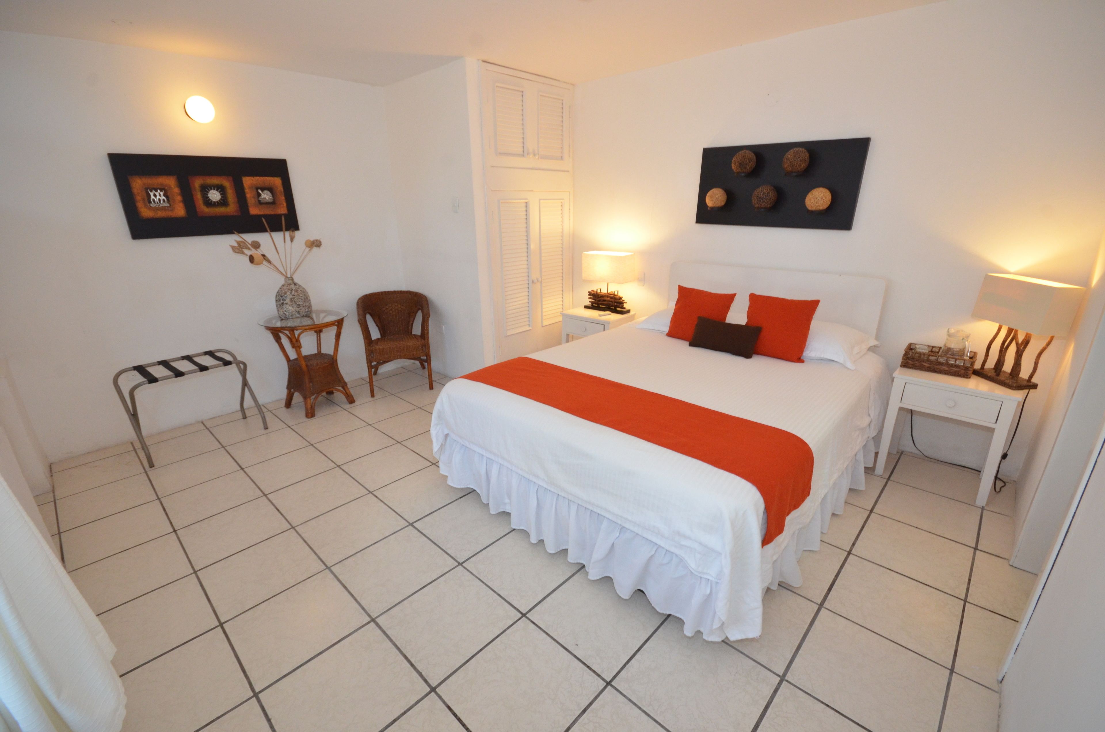 Un dormitorio ordenado con una cama grande, una silla, una mesita y una mesita de noche.