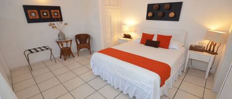 Un dormitorio ordenado con una cama grande, una silla, una mesita y una mesita de noche.