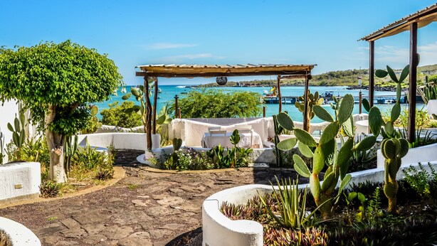 Eine Terrasse mit einer Pergola, Sitzgelegenheiten im Freien und Blick aufs Meer.