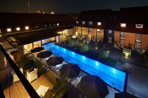 A swimming pool with lounge chairs and umbrellas, surrounded by buildings with multiple windows and a wooden deck. - Hotel Schloss Reinach (Freiburg im Breisgau)