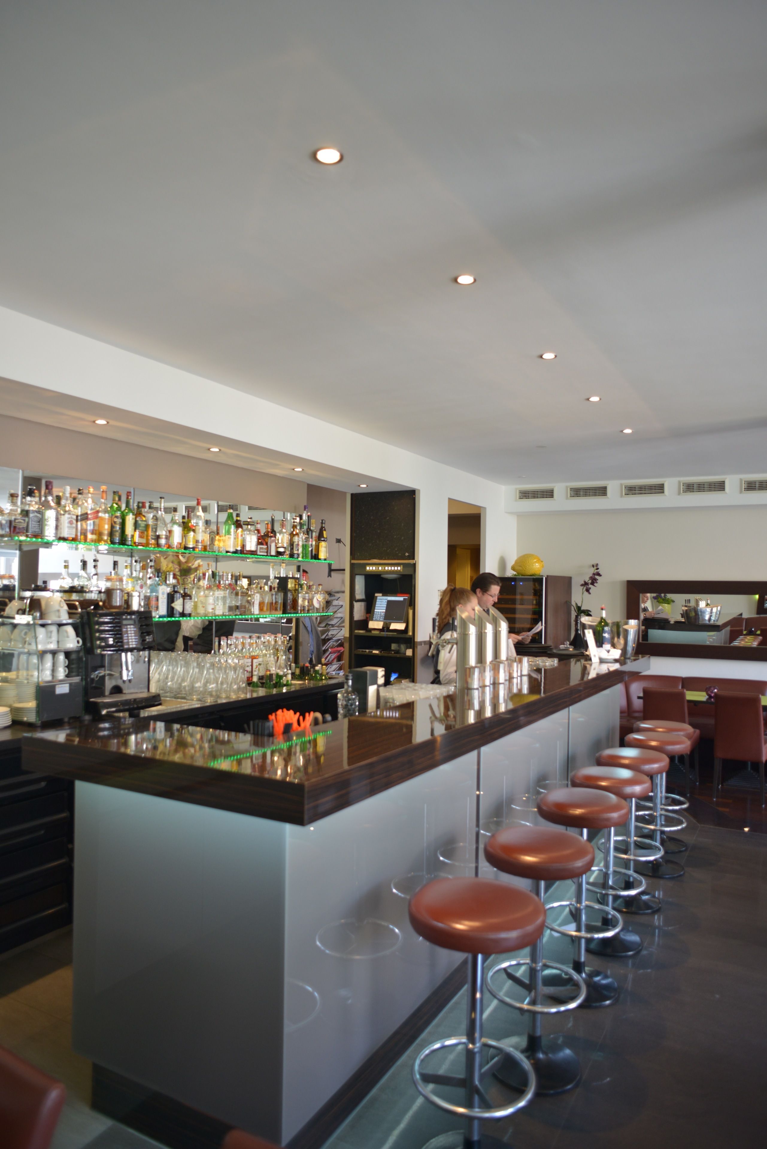 Eine Bar mit einer langen Theke, Hockern und Regalen voller Flaschen.