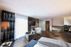 Une chambre d’hôtel moderne dotée d’un grand lit, d’un coin salon avec un canapé et un fauteuil, d’une télévision à écran plat, d’une baignoire et d’un coin repas avec une table et des chaises.