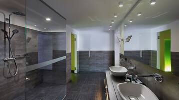 A modern bathroom with a glass-enclosed shower, a large mirror, and a vanity with a sink and bidet.