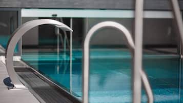 Uma piscina interior moderna com água cristalina, corrimãos de metal e uma barreira de vidro.