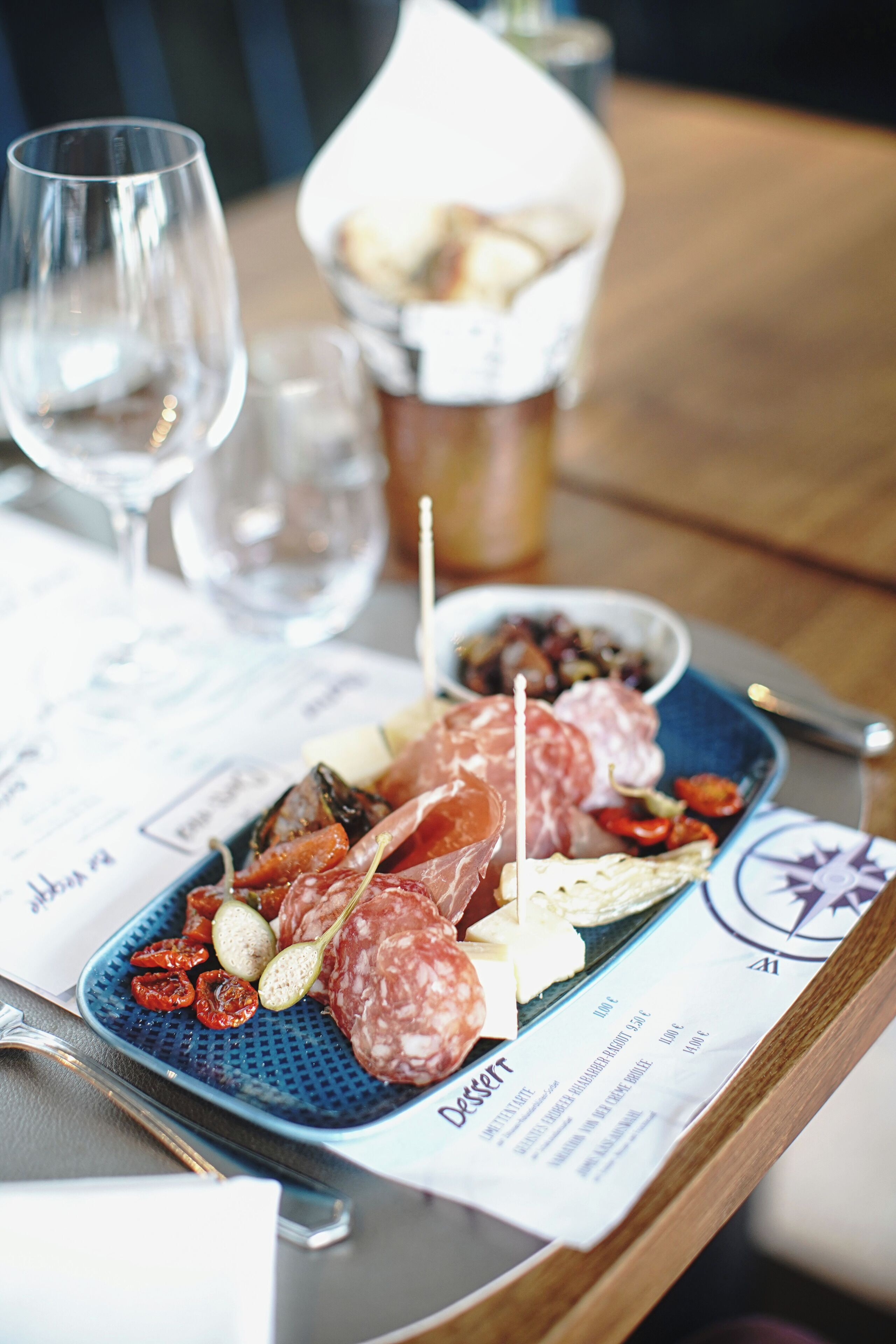 A tray with various meats, olives, and a small bowl of bread on a table with a menu.