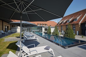 Un espace piscine aménagé sur le toit, avec des chaises longues et des parasols, entouré d’immeubles aux toits recouverts de tuiles rouges.