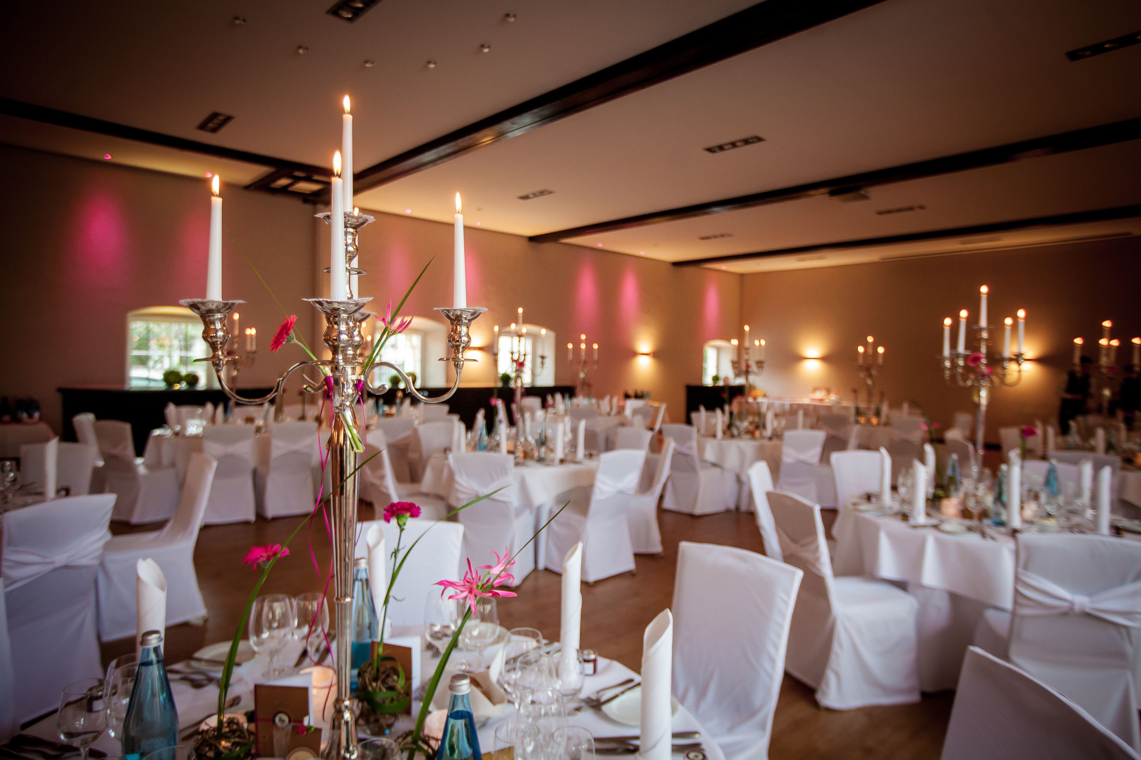 Un salón de banquetes con mesas redondas dispuestas para un evento formal, con manteles blancos, velas y centros de mesa florales.