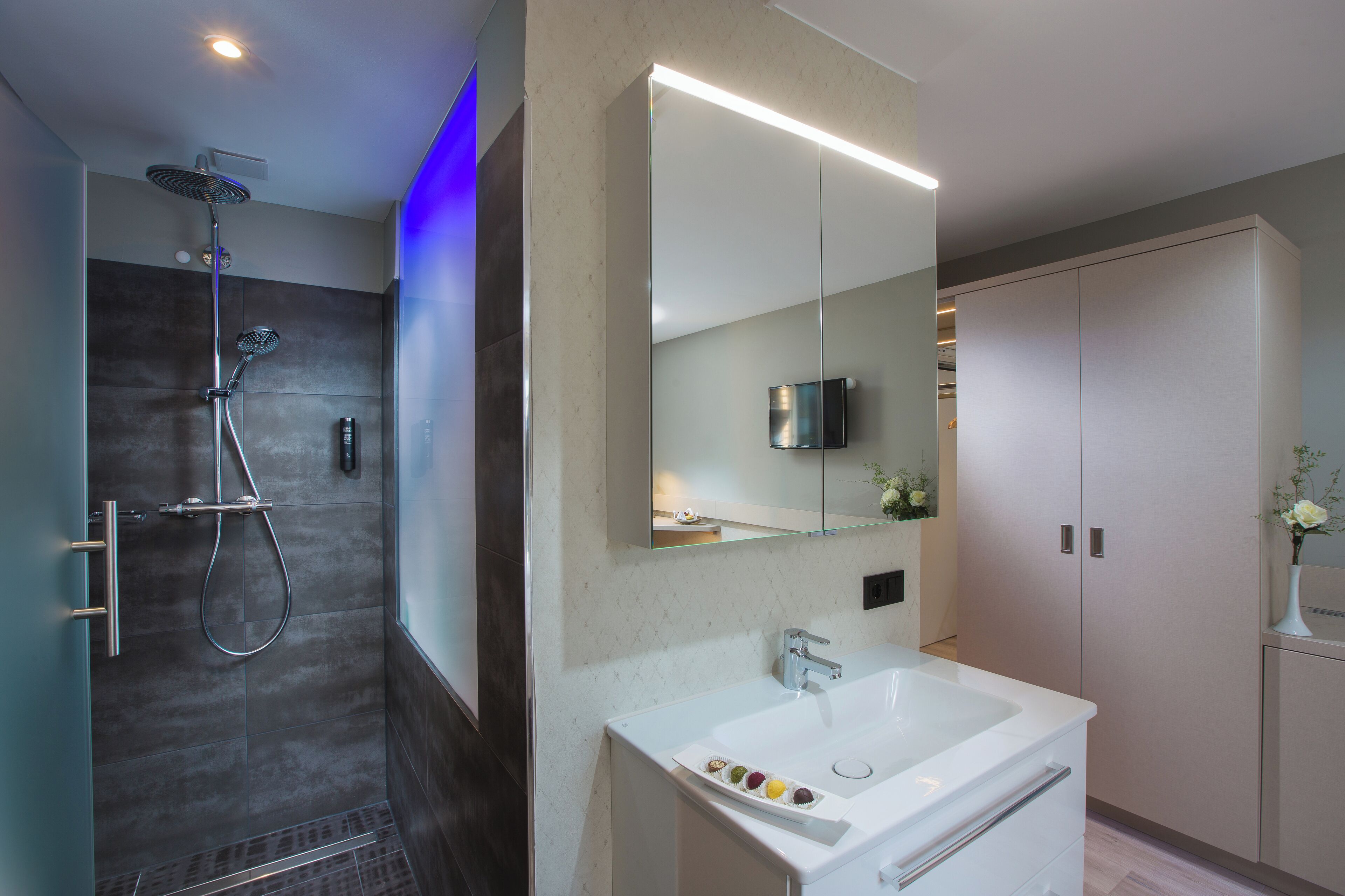 Ein modernes Badezimmer mit Dusche, einem großen Spiegel und einem weißen Waschbecken.