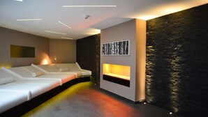 A modern spa room with a white massage table, a wall-mounted fireplace, and a stone accent wall. - Hotel Schloss Reinach (Freiburg im Breisgau)