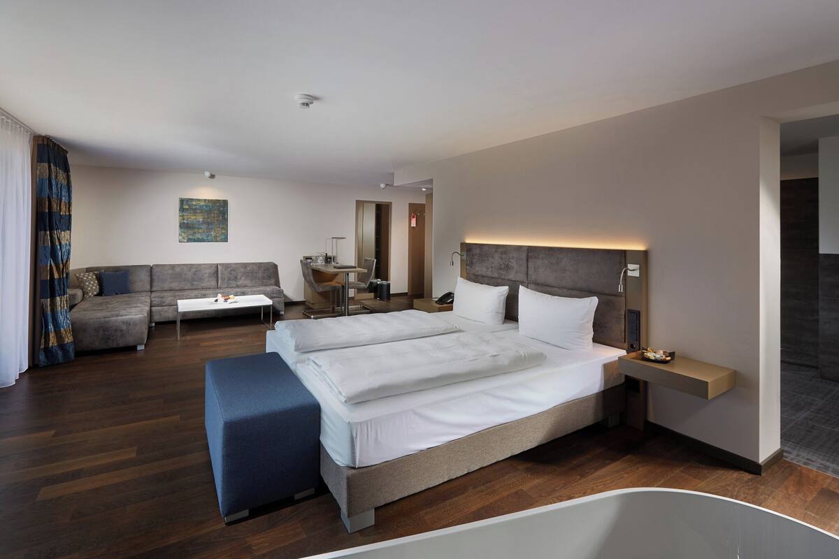 Ein modernes Hotelzimmer mit einem großen Bett, einer Couch, einem Schreibtisch und einem Badezimmer.