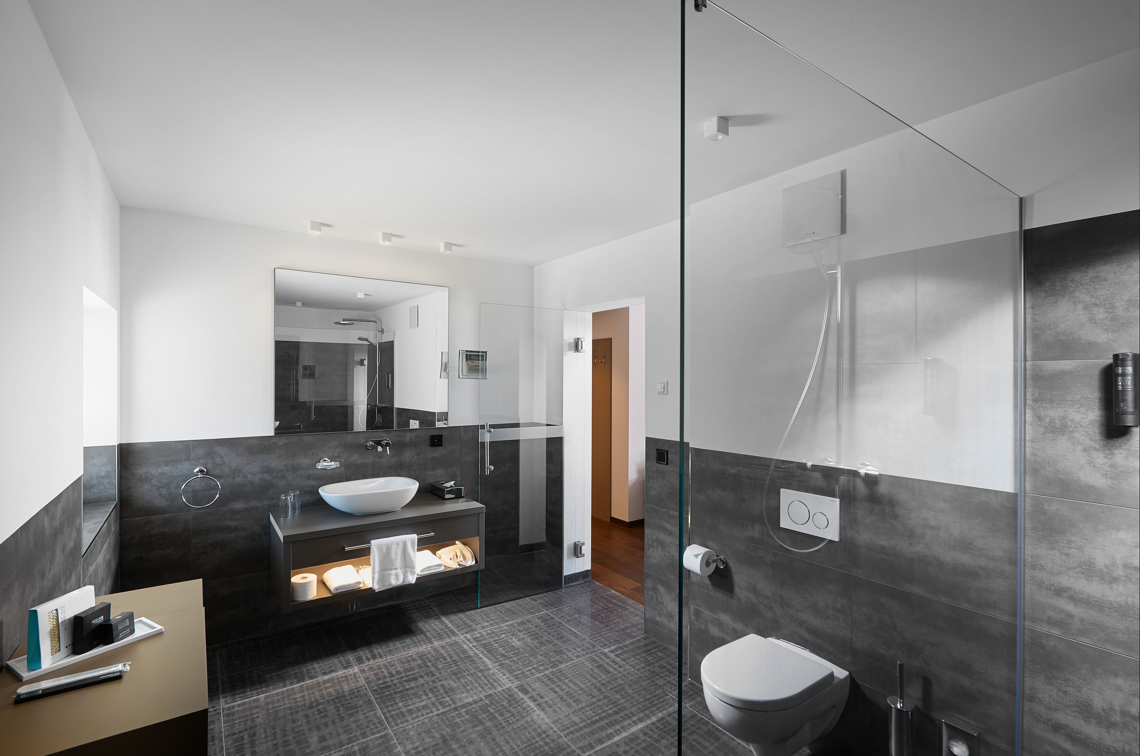 A modern bathroom with a glass shower enclosure, a large mirror, and a dark-toned vanity.