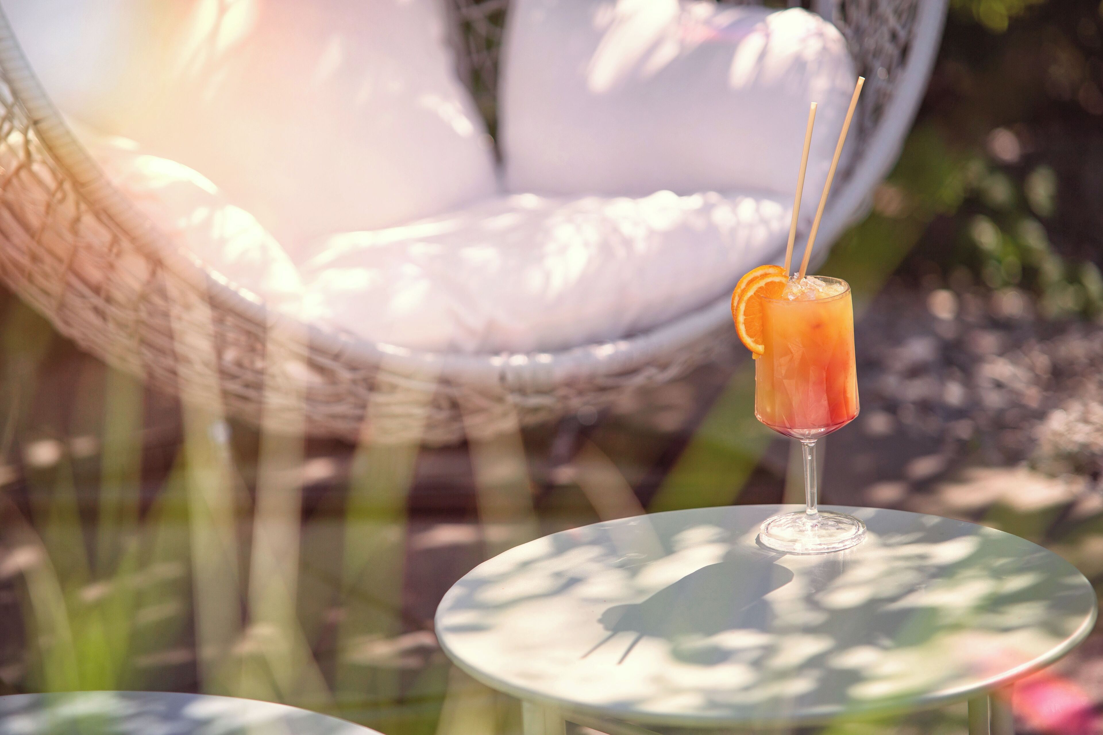 Un verre contenant une boisson, agrémenté d’une tranche d’orange, est posé sur une table ronde à l’extérieur.