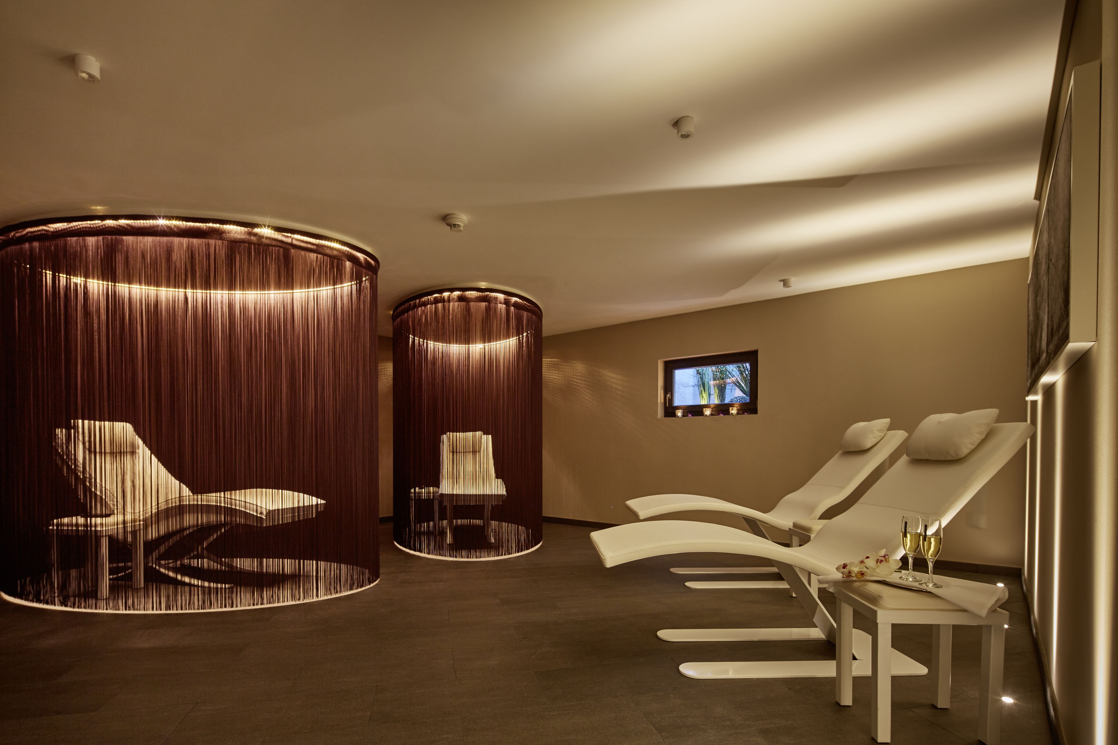 Une salle de spa équipée de deux fauteuils inclinables, d’une petite table avec un plateau et des verres, et d’un téléviseur fixé au mur.