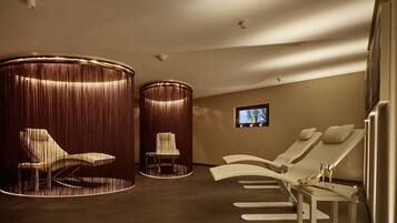 Une salle de spa équipée de deux fauteuils inclinables, d’une petite table avec un plateau et des verres, et d’un téléviseur fixé au mur.