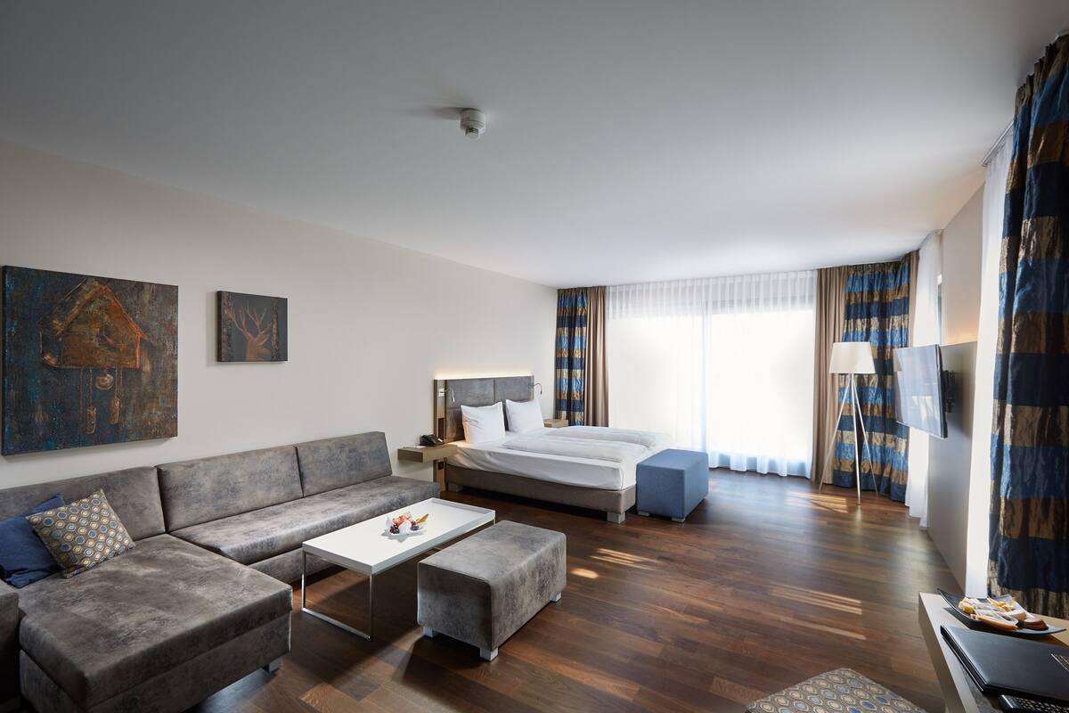 Ein modernes Hotelzimmer mit einer Couch, einem Bett, einem kleinen Tisch und einem Fernseher.