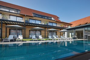 Une piscine avec des chaises longues et des parasols, un bâtiment en bois avec un toit rouge et de grandes fenêtres.