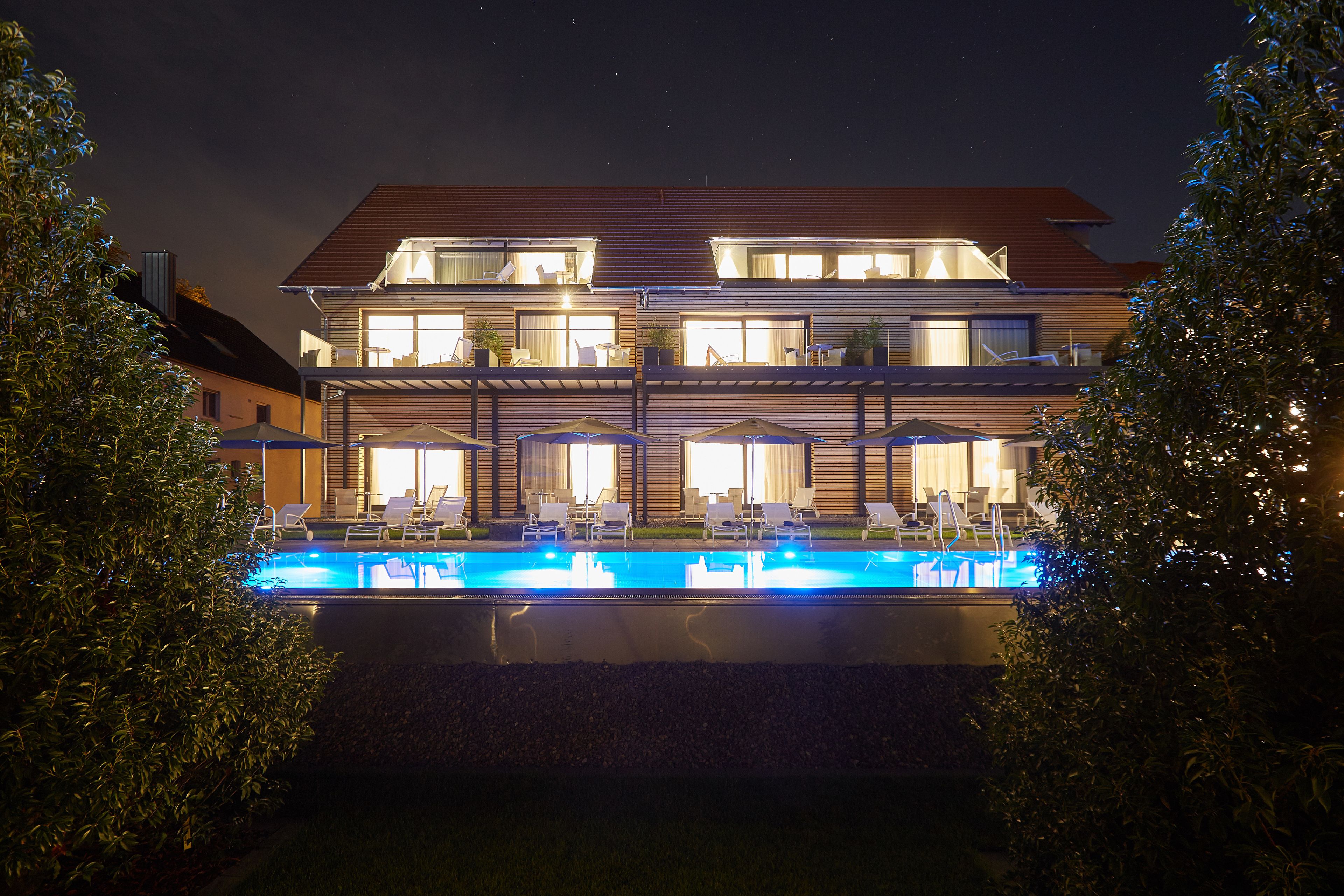 A two-story building with a swimming pool, lounge chairs, and umbrellas.