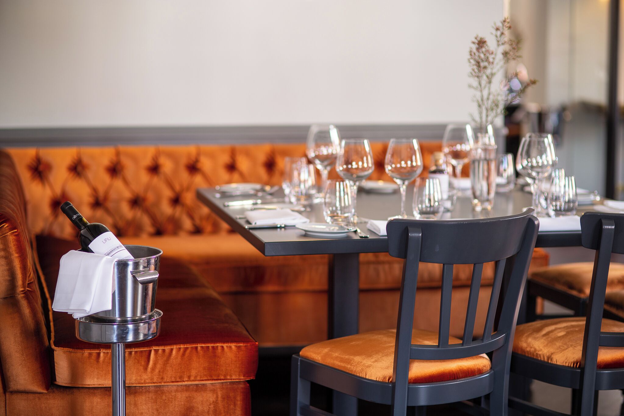 Un comedor con una banca de madera, una mesa dispuesta con copas de vino, platos y cubiertos.