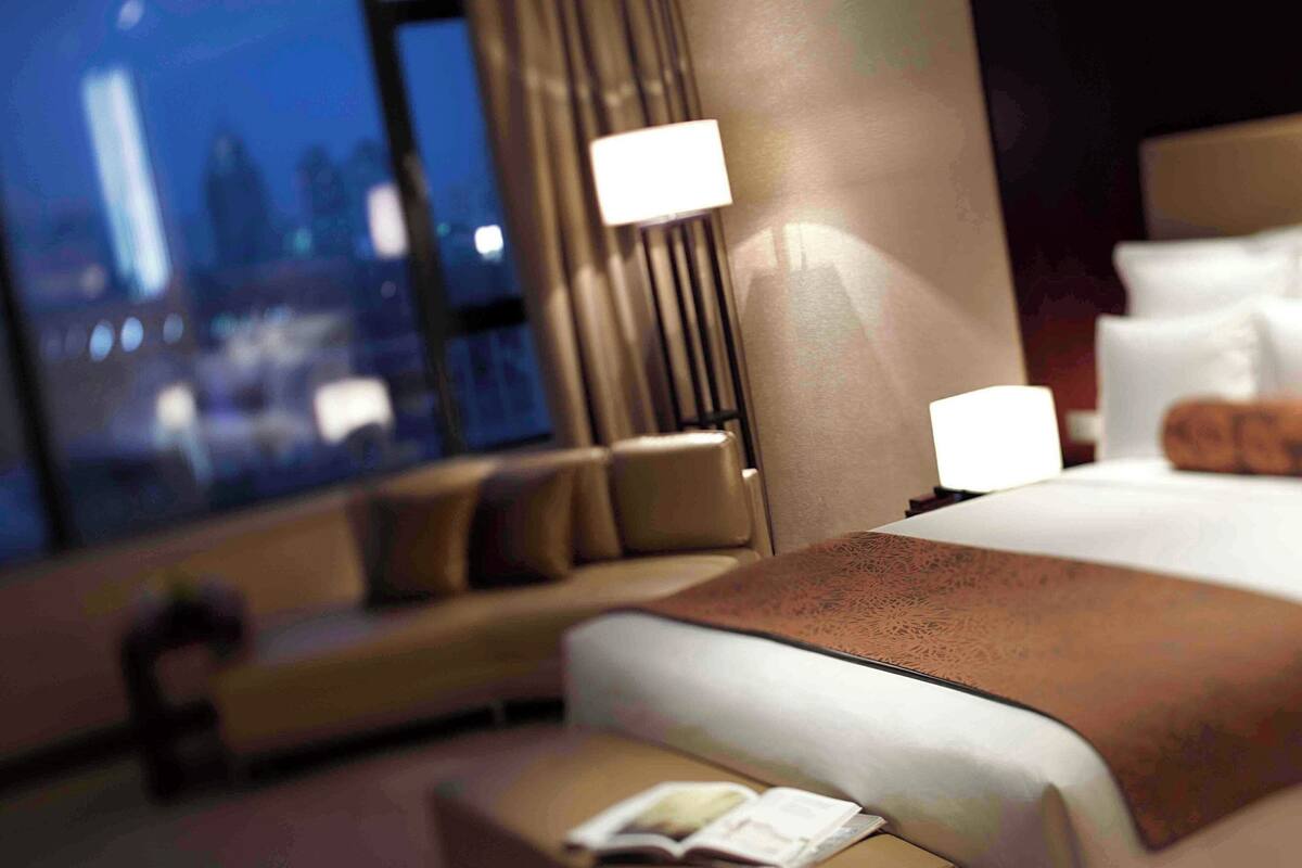 A hotel room with a large bed, a sofa, and a nightstand with a lamp.