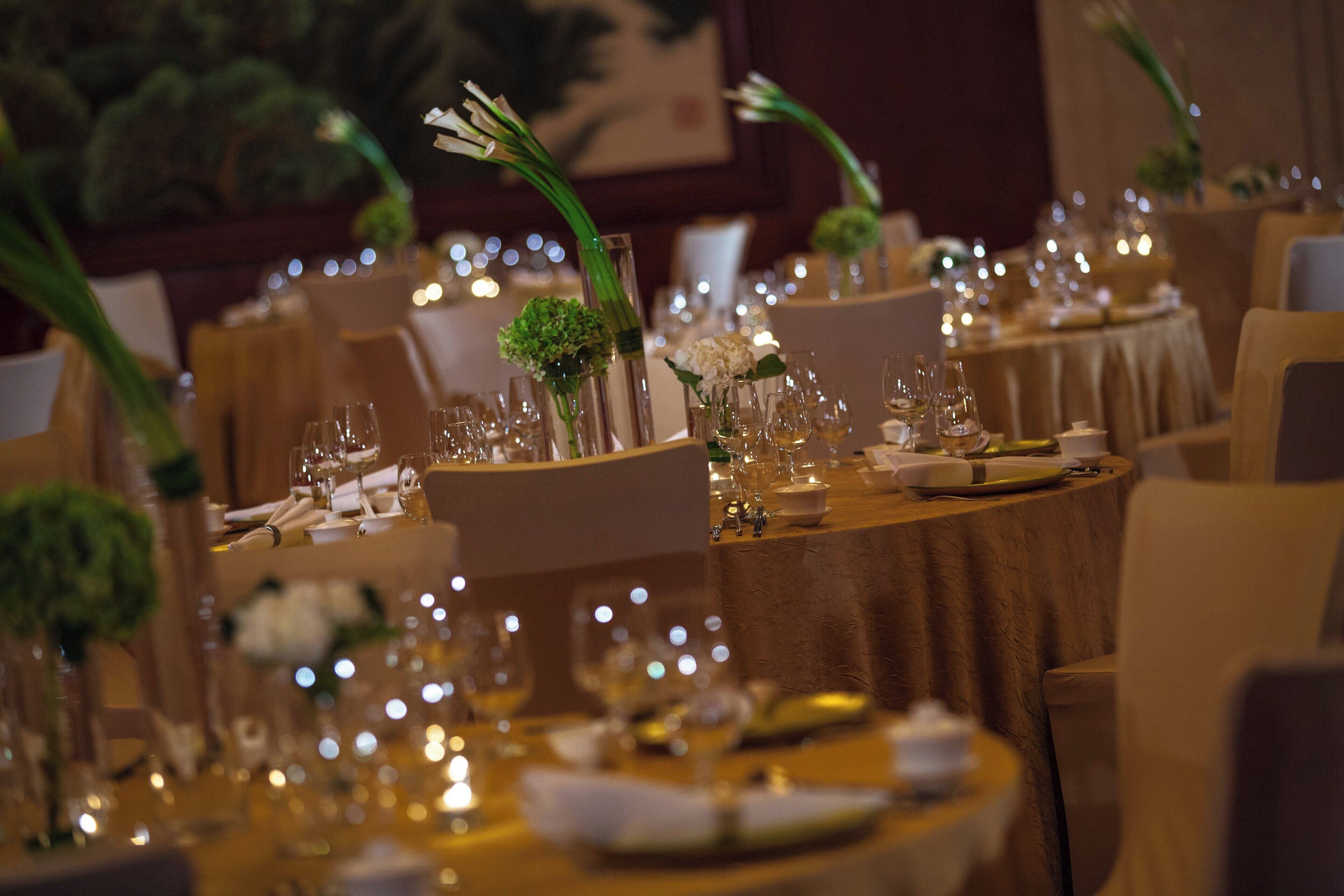 A banquet hall with round tables set for a formal event, featuring floral centerpieces and fine china.