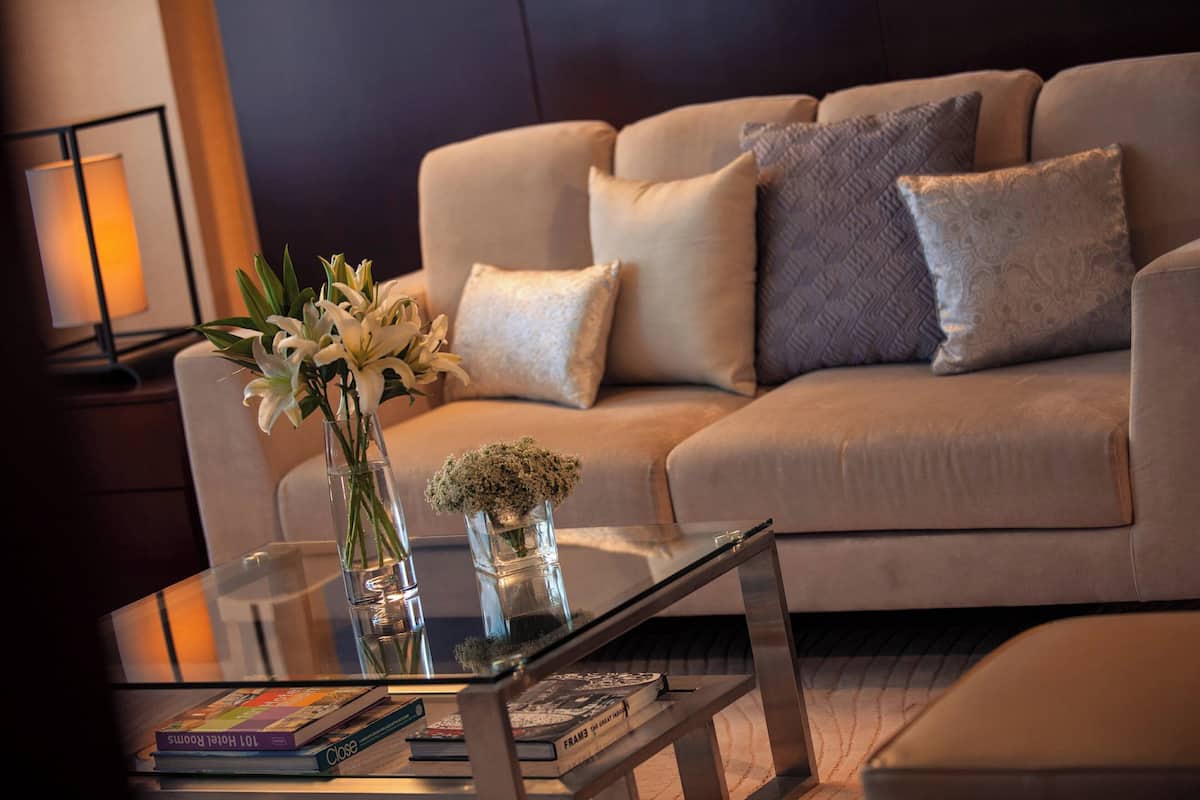 A modern living room with a beige sofa, a glass coffee table, and a vase with flowers.