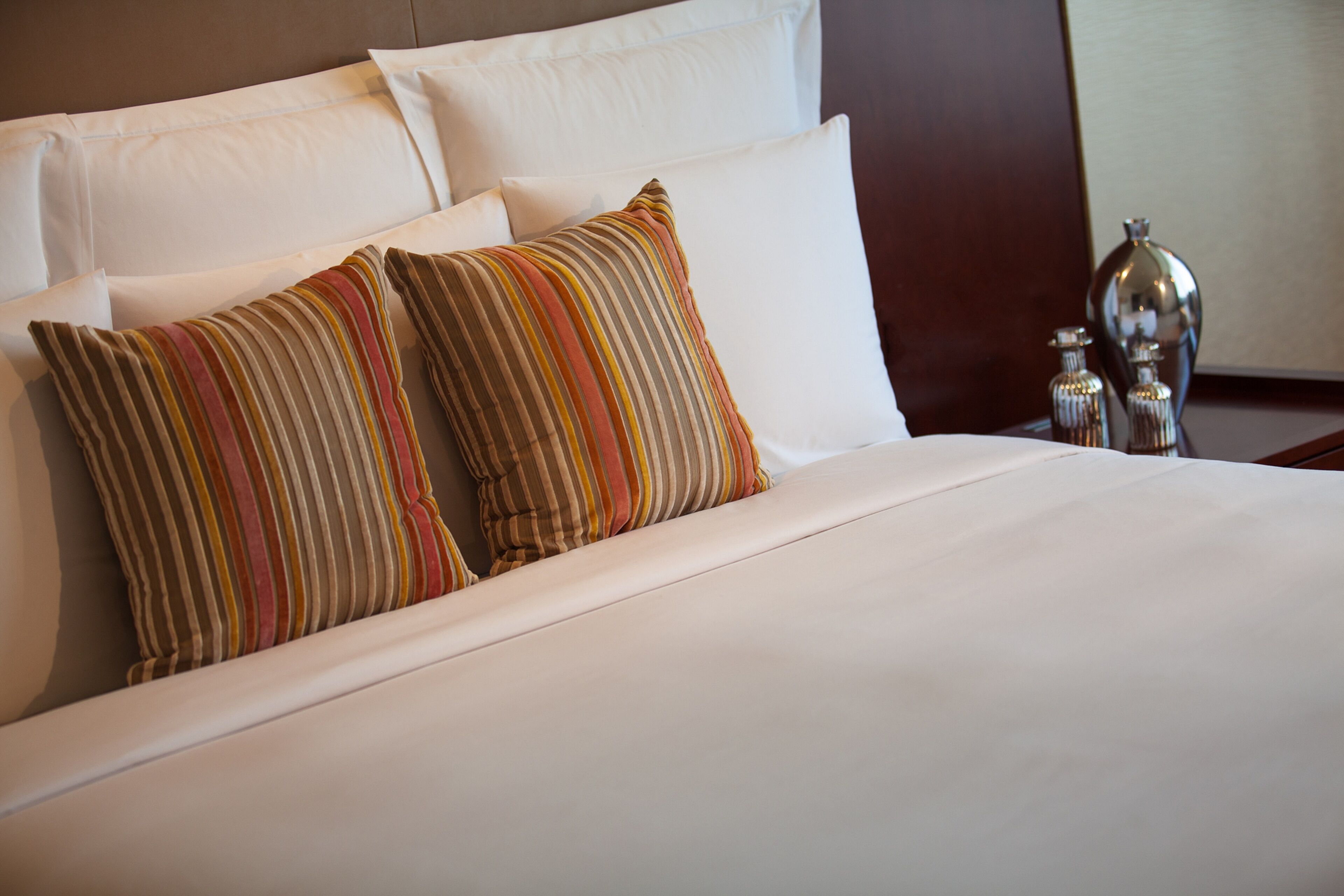 A neatly made bed with white linens and two striped pillows.