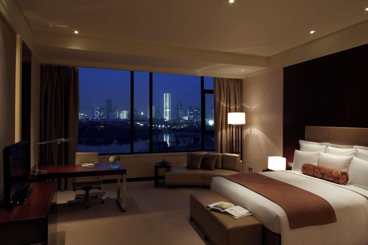 A hotel room with a large window, a bed, a desk, and a chair.